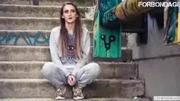 Kira Parvati mit langem braunem Haar und verzweifeltem Gesichtsausdruck vor bunter Graffiti-Wand